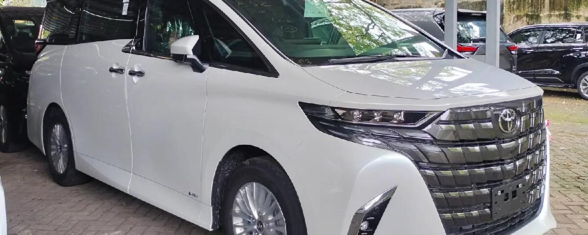 White minivan parked under a metal carport with other vehicles nearby, in a paved lot.