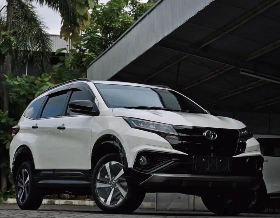 Front-left three-quarter view of a white Toyota SUV parked outdoors near a metal-roofed structure and greenery.