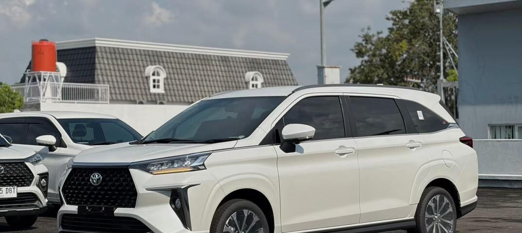 Front three-quarter view of a white SUV parked in a lot on a sunny day, with other vehicles in the background and clear sky above.