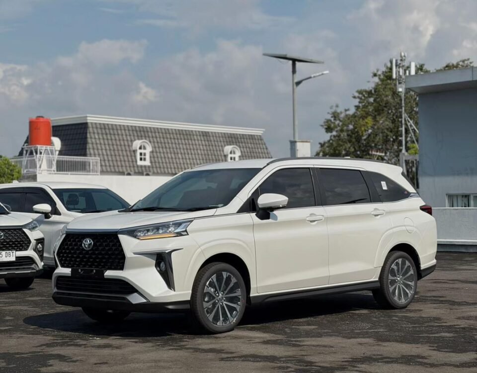 Front three-quarter view of a white SUV parked in a lot on a sunny day, with other vehicles in the background and clear sky above.