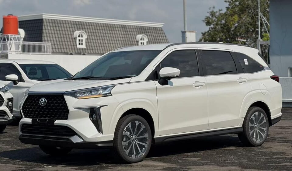 Front three-quarter view of a white SUV parked in a lot on a sunny day, with other vehicles in the background and clear sky above.