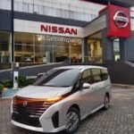 SaveTikTokto_7491337582182141192_2 - Dyantransport Silver Nissan minivan parked in front of a Nissan dealership with a glass showroom and large red Nissan sign above the entrance.