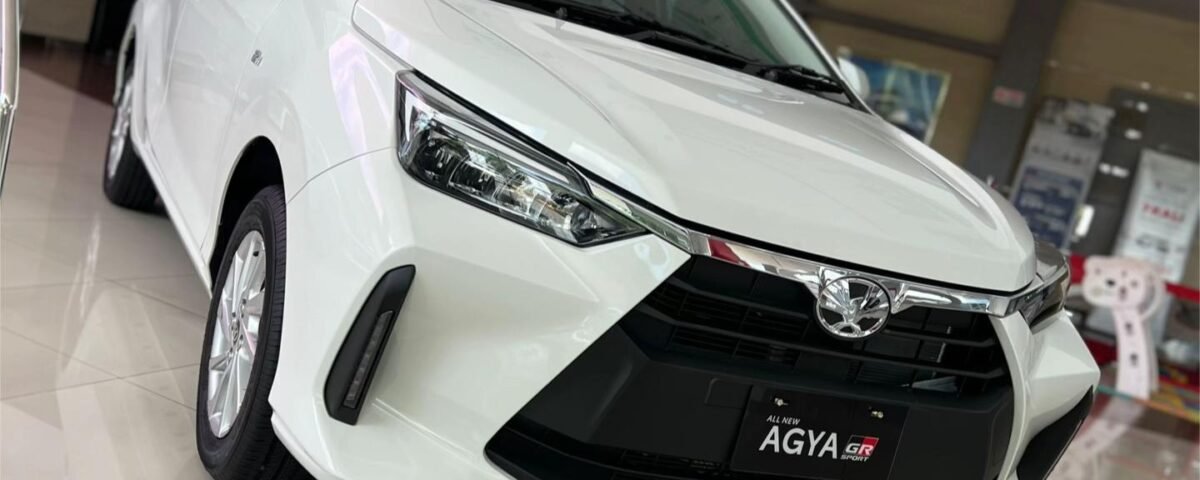 SaveTikTokto_7494885108328025399_2 - Dyantransport White Toyota Agya GR Sport on a showroom floor, angled front view with glossy tiles and showroom signage in the background
