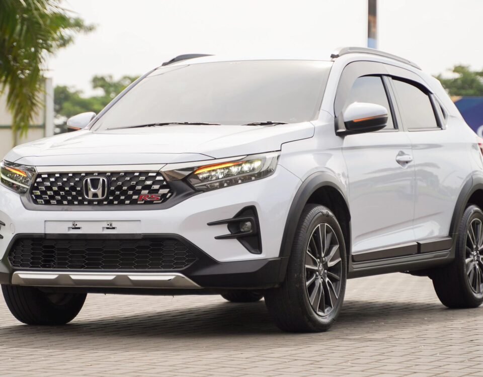 White Honda SUV three-quarter front view, RS badge visible, parked on a paved lot with greenery in background