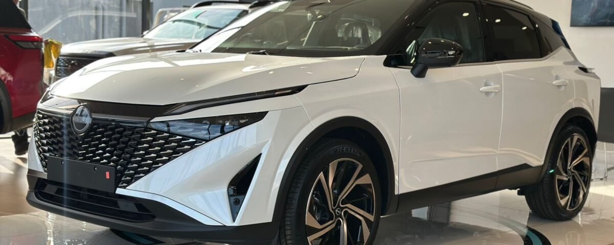 White Nissan SUV on a dealership showroom floor, front-left view with bold black grille and big alloy wheels.