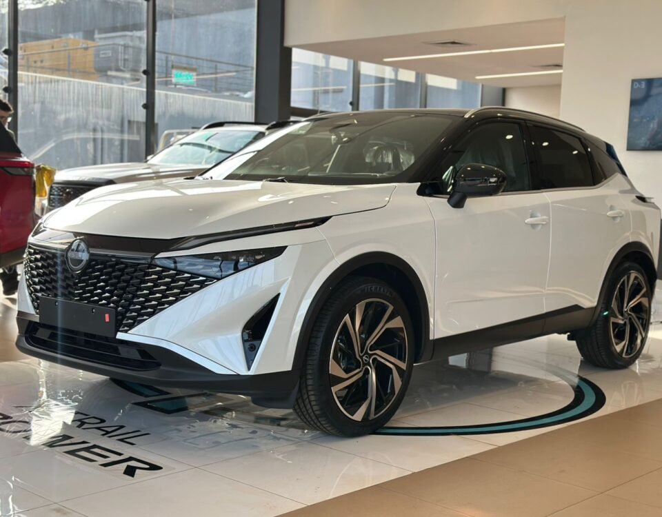 White Nissan SUV on a dealership showroom floor, front-left view with bold black grille and big alloy wheels.