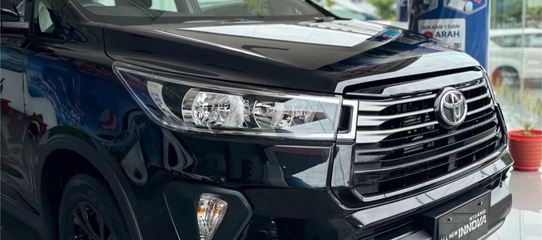 Front three-quarter view of a black Toyota Innova in a showroom, showcasing the chrome grille and headlamps.