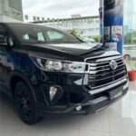 Front three-quarter view of a black Toyota Innova in a showroom, showcasing the chrome grille and headlamps.
