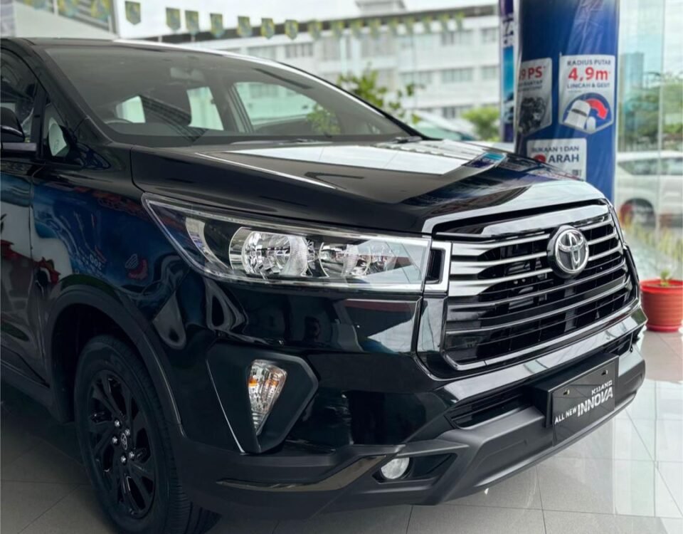 Front three-quarter view of a black Toyota Innova in a showroom, showcasing the chrome grille and headlamps.