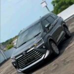 Gray SUV photographed from the front-left angle on a paved outdoor area under a blue sky.