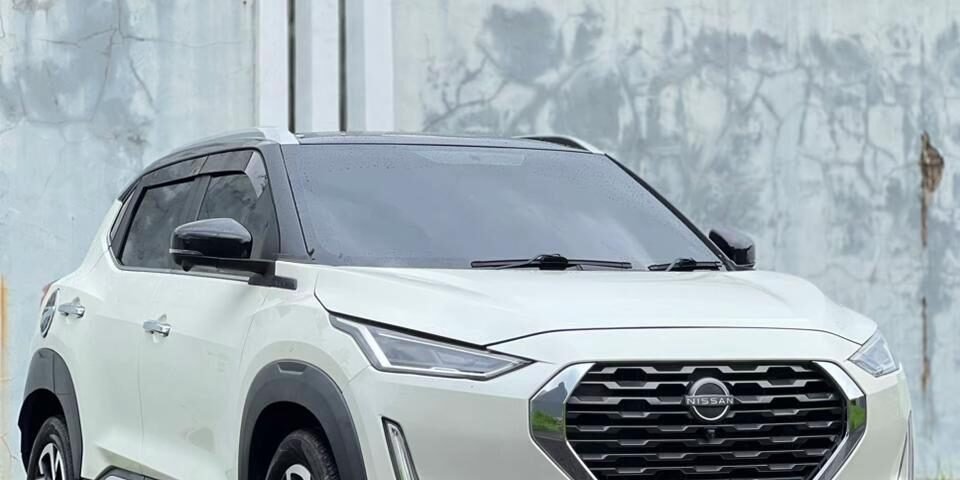 White Nissan SUV parked on a wet road, front three-quarter view, gray concrete wall behind.