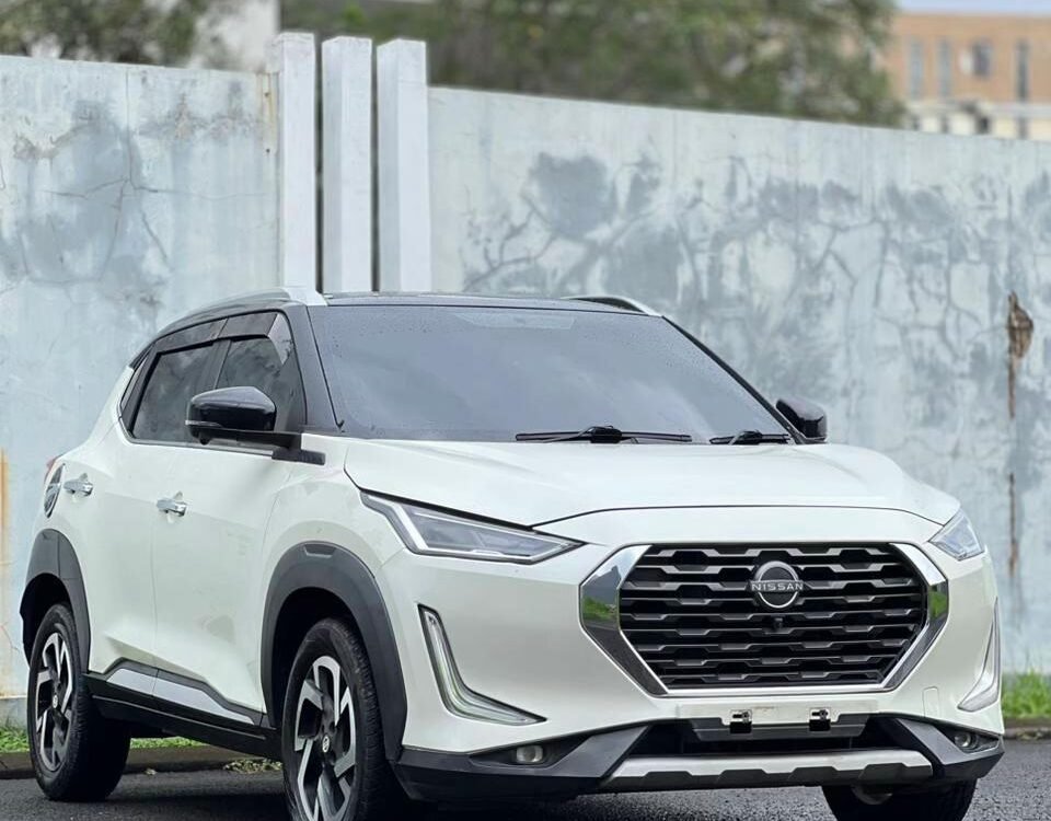 White Nissan SUV parked on a wet road, front three-quarter view, gray concrete wall behind.