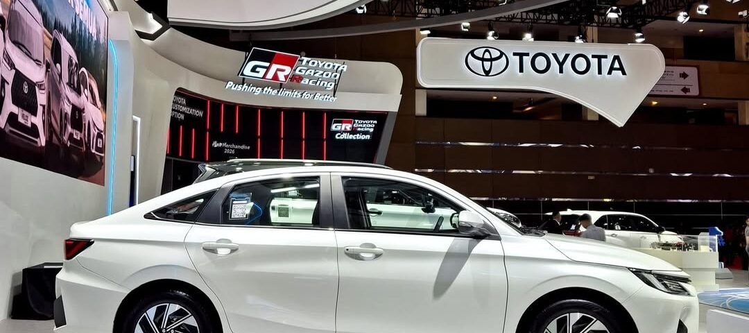 SaveTikTokto_7603938007632170258_3 - Dyantransport White sedan on a pedestal at an auto show, with a prominent Toyota booth and futuristic curved architecture overhead