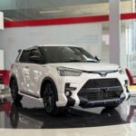 White Toyota SUV on a glossy showroom floor with red seating and glass walls behind it, angled to show front and side.