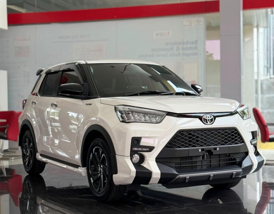 White Toyota SUV on a glossy showroom floor with red seating and glass walls behind it, angled to show front and side.