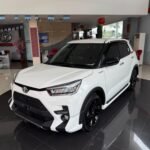 SaveTikTokto_7607337355426450696_2 - Dyantransport White Toyota SUV on a glossy showroom floor, front three-quarter view with black wheels and tinted windows, dealership interior in the background.