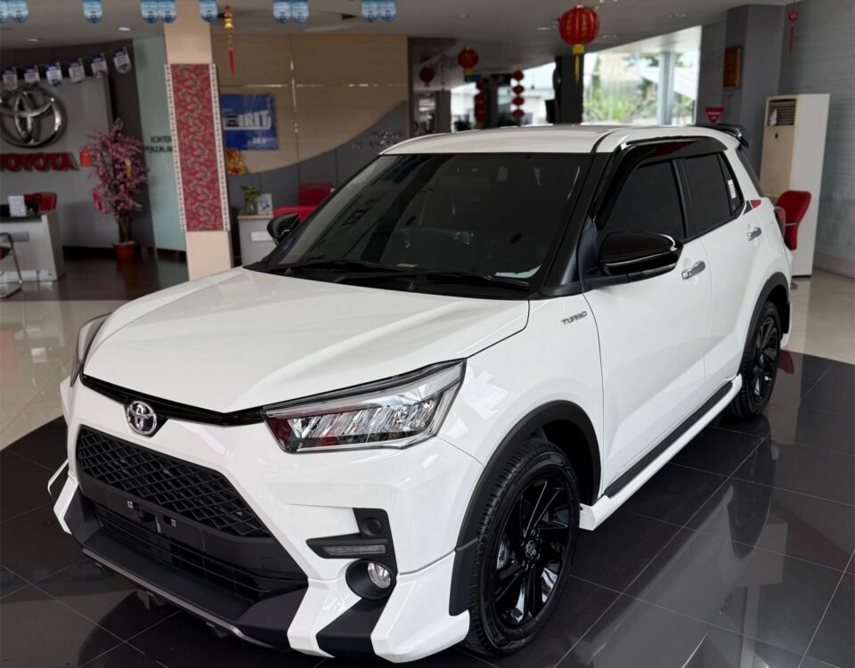 SaveTikTokto_7607337355426450696_2 - Dyantransport White Toyota SUV on a glossy showroom floor, front three-quarter view with black wheels and tinted windows, dealership interior in the background.