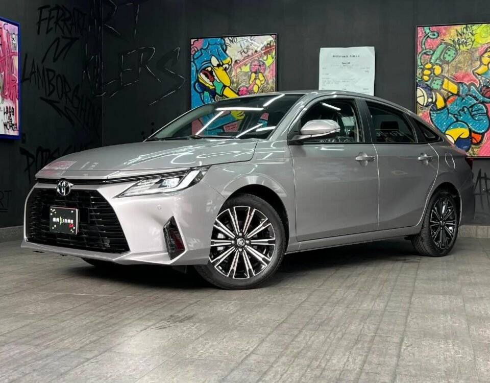 Grey sedan displayed indoors in a modern showroom, with graffiti artwork on black walls and bright linear light fixtures above.
