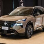 Silver Nissan X-Trail SUV on a showroom floor, facing left, with blue LED headlights and a bold front grille.