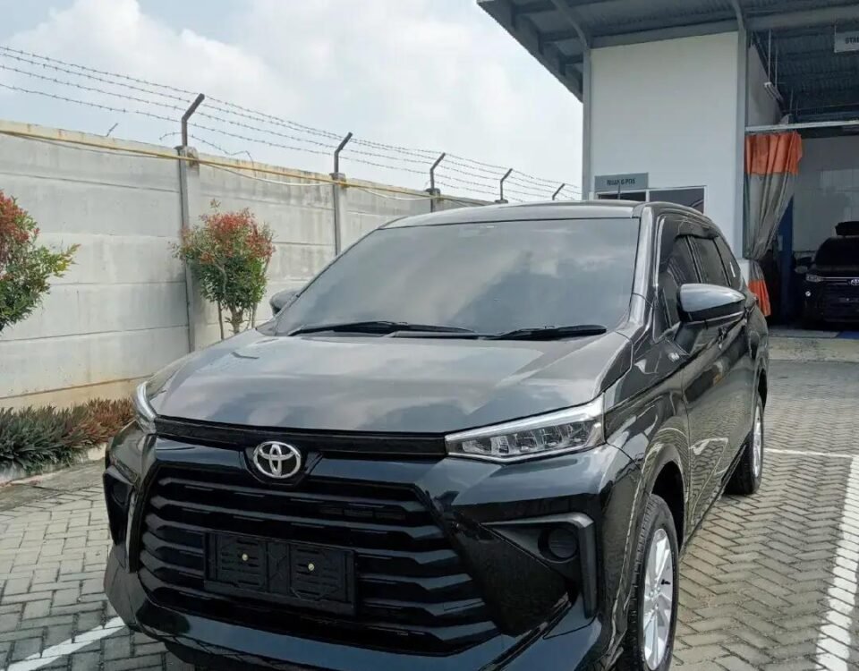 Front three-quarter view of a dark gray Toyota SUV parked in a lot near a service building with a barbed-wire fence behind it.