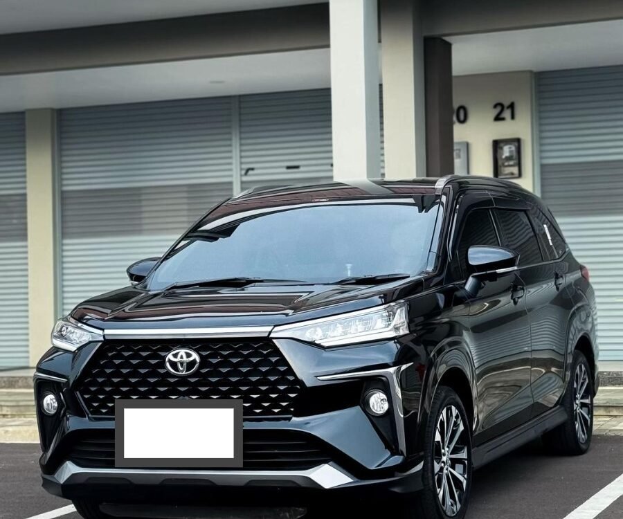 Front three-quarter view of a black Toyota SUV parked in a lot in front of a modern building with shuttered storefronts; prominent grille and headlights visible.