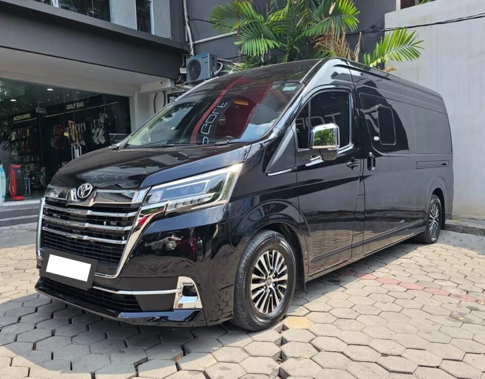 Black Toyota van parked on a hexagonal-paver driveway in front of a storefront with palm trees overhead at street level.