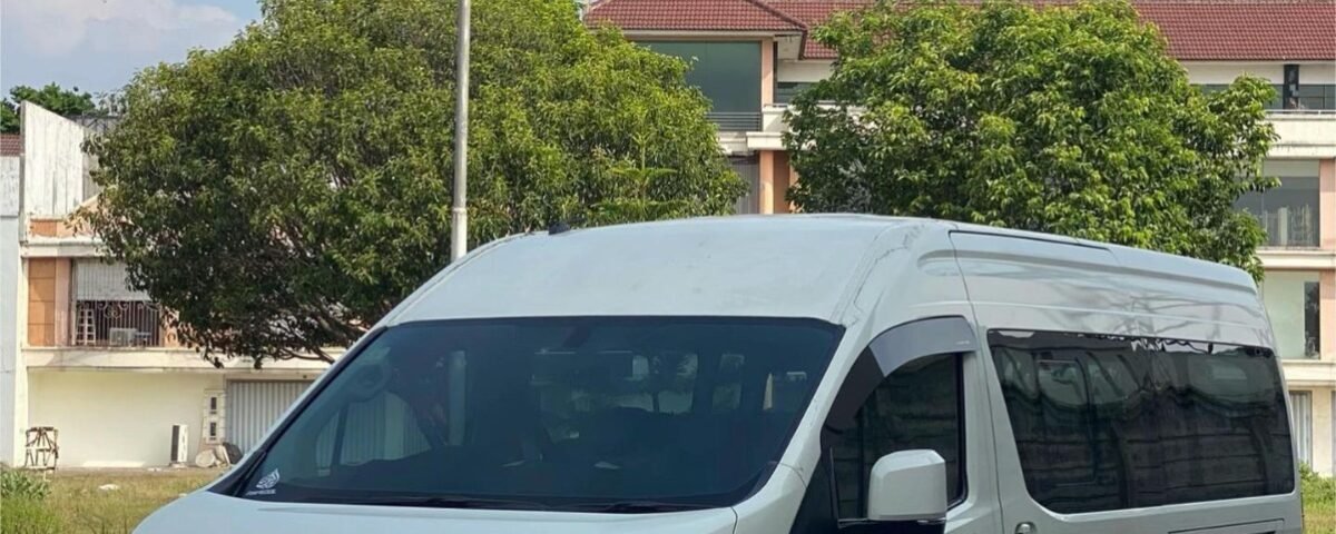 Front three-quarter view of a white Toyota van parked on a brick-paved lot with trees and buildings in the background.