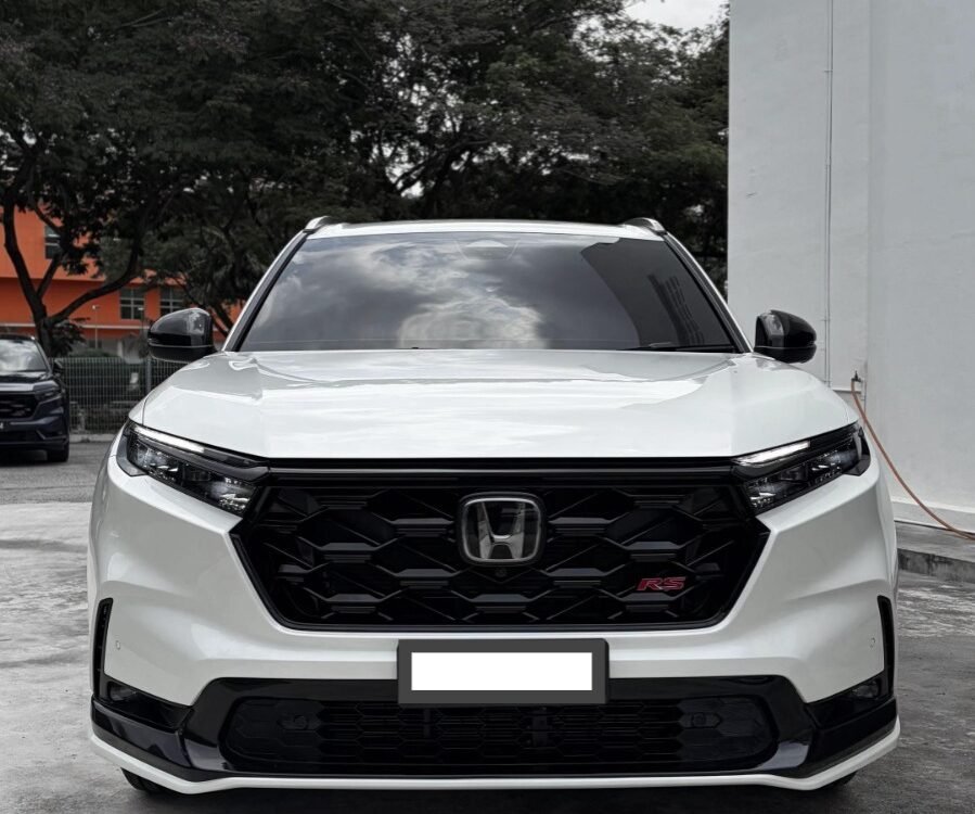 Front view of a white Honda SUV (RS trim) parked on a concrete lot, showing bold black grille and emblem.