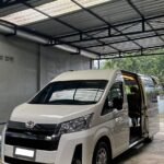 White Toyota van parked inside a metal-carport with the side door open, revealing beige interior seats.