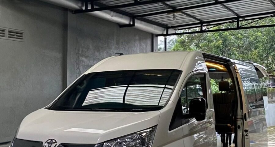White Toyota van parked inside a metal-carport with the side door open, revealing beige interior seats.