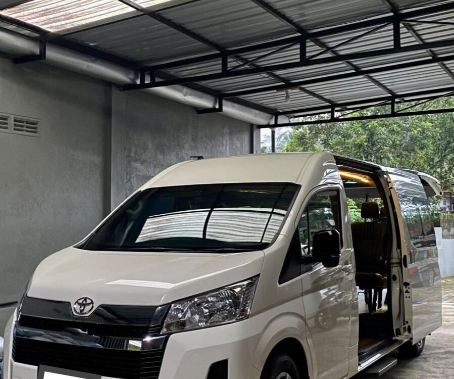 White Toyota van parked inside a metal-carport with the side door open, revealing beige interior seats.