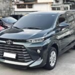 Gray Toyota SUV parked in a lot, showing the front grille and headlights with other cars in the background.
