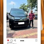WhatsApp Image 2026-08-20 at 121706 - Dyantransport Man standing beside a black Toyota van in a parking lot; pickup service post for Semarang.