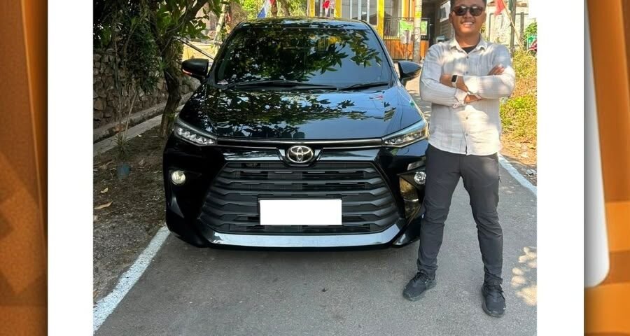 Man standing with arms crossed beside a black Toyota SUV in a parking area with festive bunting