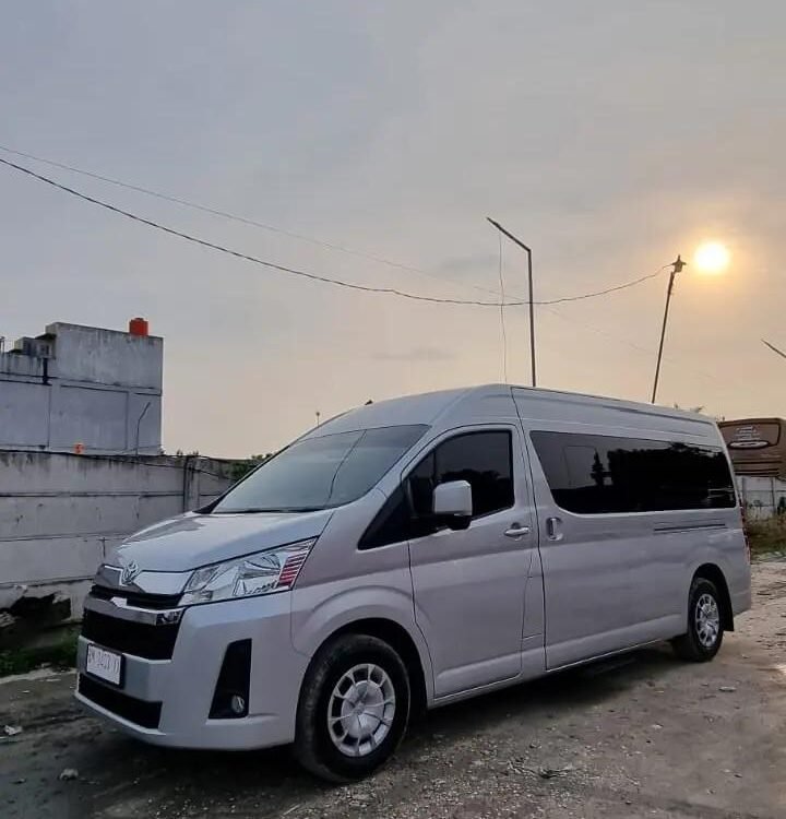 White modern van parked on a dirt lot beside a low wall, with a sunset sky and streetlight in the background.