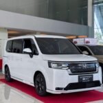 snaptik-app-7534650141228174598-slide-1 - Dyantransport White Honda StepWGN minivan on a glossy showroom floor with a red carpet and large glass windows in the background.
