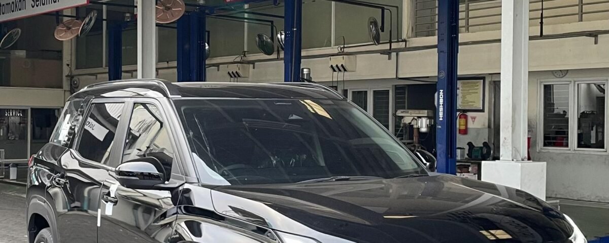 snaptik-app-7543229055034871047-slide-1 - Dyantransport Black SUV parked inside a service bay with a 'Dilarang Merokok' (No Smoking) sign overhead, industrial lights above.