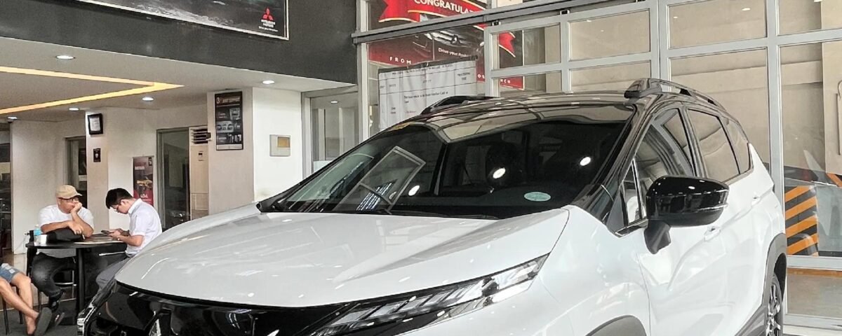 snaptik-app-7572045462241316104-slide-3 - Dyantransport White Mitsubishi Xpander Cross SUV on display in a dealership showroom with glass-walled offices behind it.