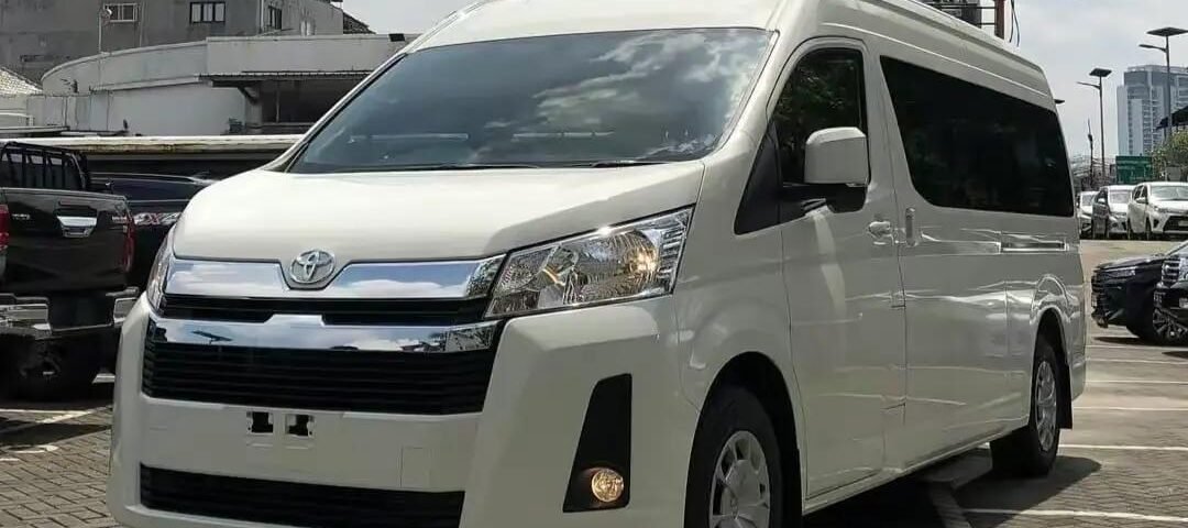 White Toyota van parked in a lot with other vehicles and urban buildings in the background.