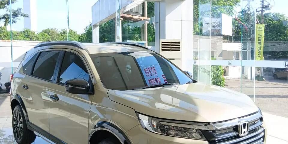 snaptik-app-7584003140563864850-slide-2 - Dyantransport Beige Honda BR-V N7X on display in a bright showroom, shown from the front-three-quarters with glass walls and a glossy tiled floor.