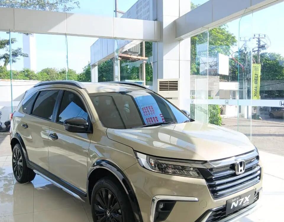 Beige Honda BR-V N7X on display in a bright showroom, shown from the front-three-quarters with glass walls and a glossy tiled floor.
