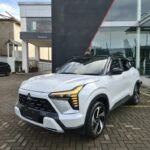 White Mitsubishi SUV parked on a brick driveway in front of a modern dealership building.] ,