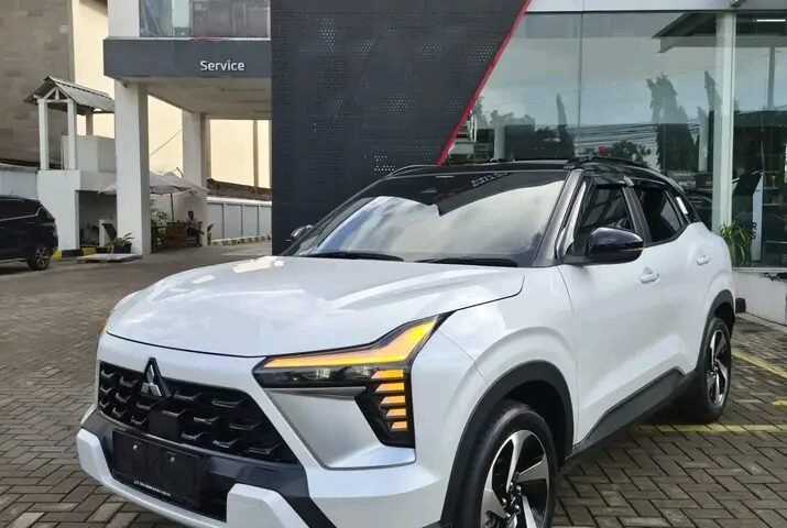 White Mitsubishi SUV parked on a brick driveway in front of a modern dealership building.] ,