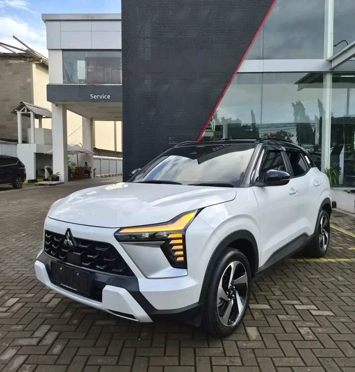 White Mitsubishi SUV parked on a brick driveway in front of a modern dealership building.] ,