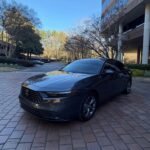 Black Honda sedan parked on brick driveway in front of a modern glass-front building on a sunny day