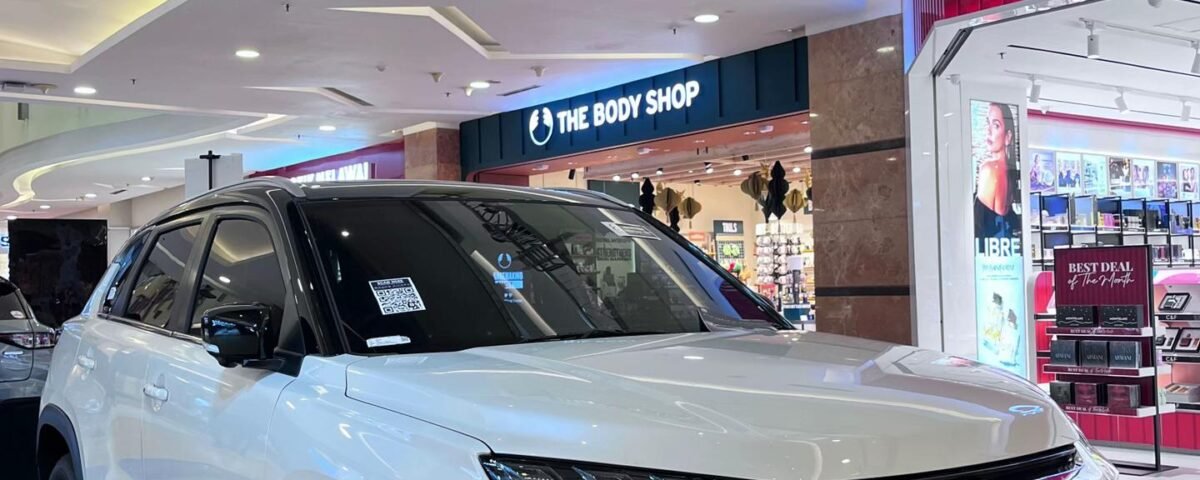 White Suzuki Grand Vitara SUV on a showroom platform inside a shopping mall with The Body Shop storefront in the background.] ,