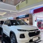 White Suzuki Grand Vitara SUV on a showroom platform inside a shopping mall with The Body Shop storefront in the background.] ,