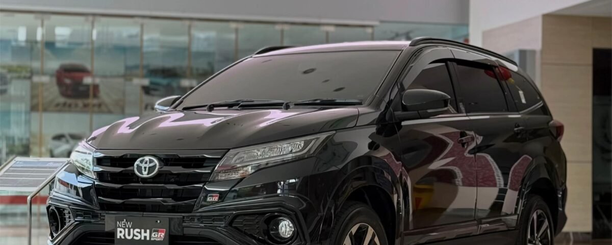 Front three-quarter view of a black Toyota SUV on a bright showroom floor, with the 'New Rush GR' badge on the grille.