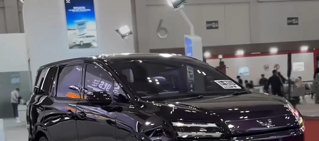 Black multi-purpose vehicle on a showroom floor with a large DARION EV sign in front and bright exhibition lights above.