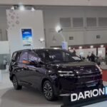 Black multi-purpose vehicle on a showroom floor with a large DARION EV sign in front and bright exhibition lights above.